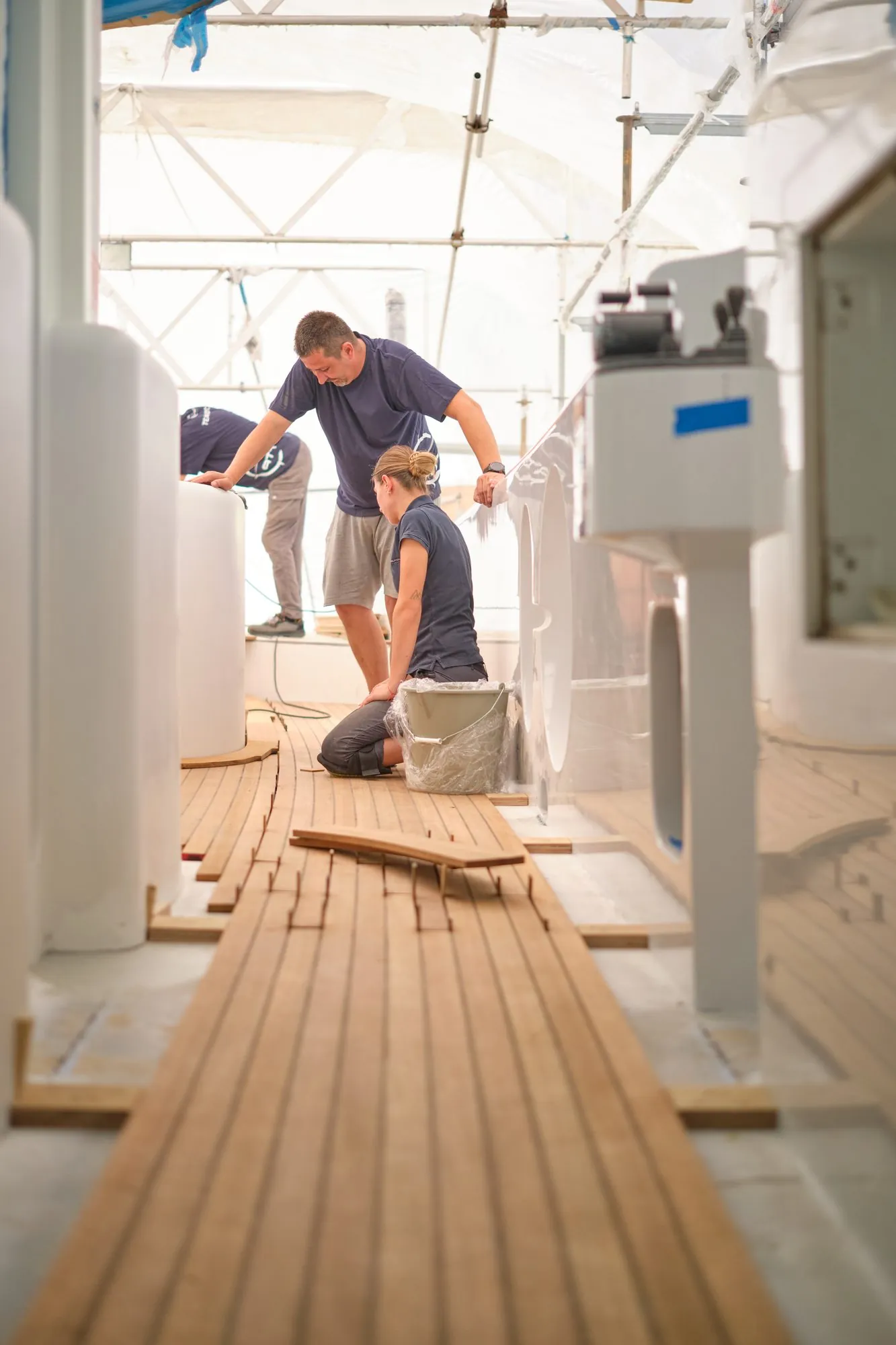 Two ATT Nautica fitters laying teak panels on the side deck of a Rossinavi 46 under scaffolding