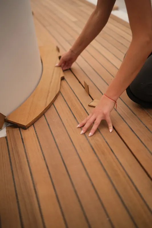 Hands fitting a curved teak margin plank around a deck fitting